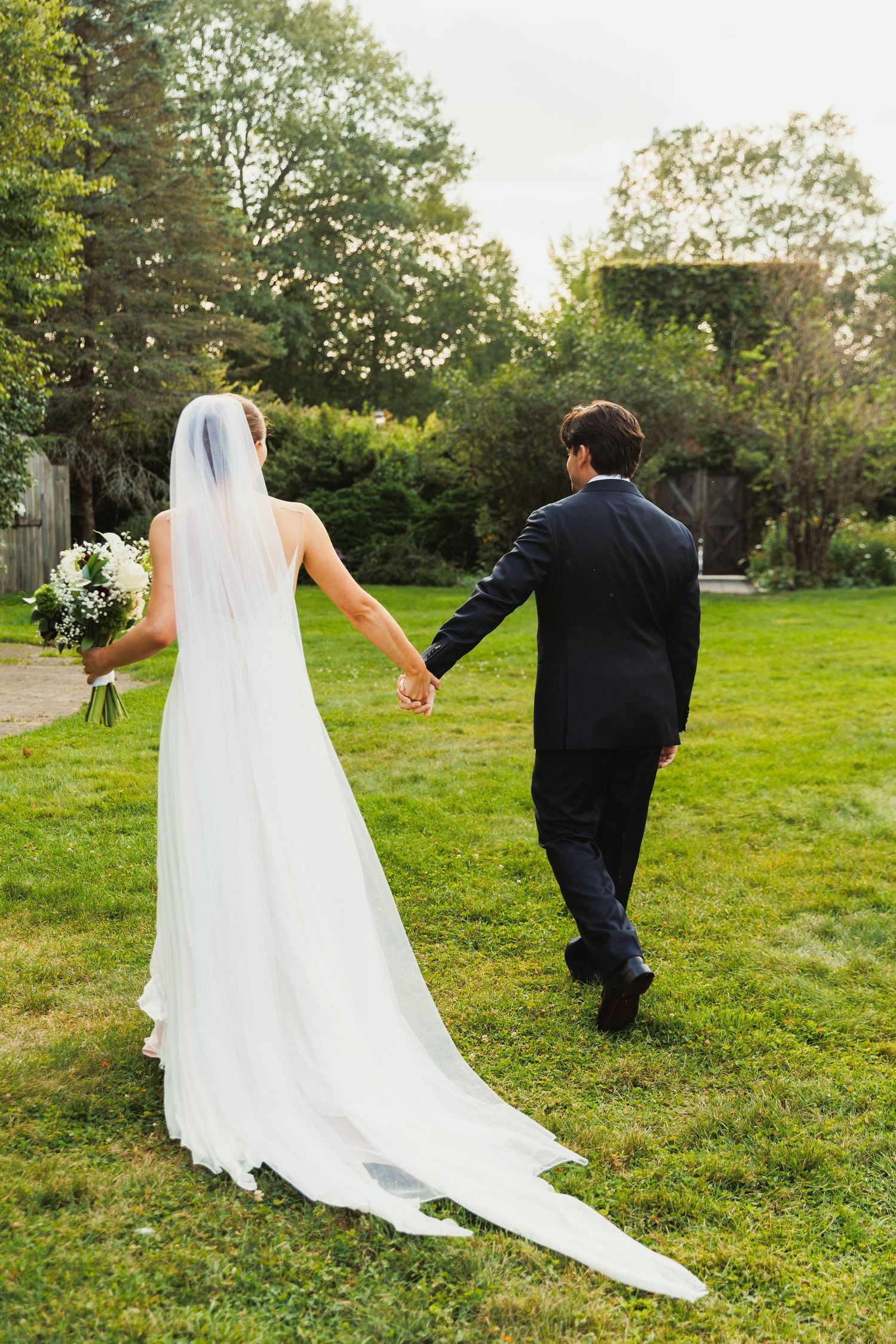 A couple walks playfully through a green garden during their wedding photoshoot.