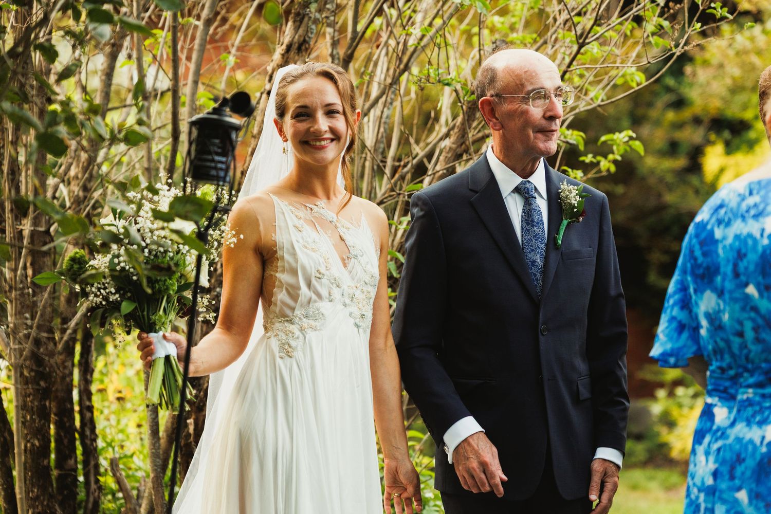 Wedding party walks through a lush garden path during an outdoor celebration.