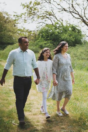 A family walks together holding hands along a grassy trail on a bright summer day.