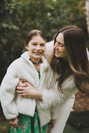 A mother and daughter share a joyful moment outdoors wearing cozy white winter jackets.