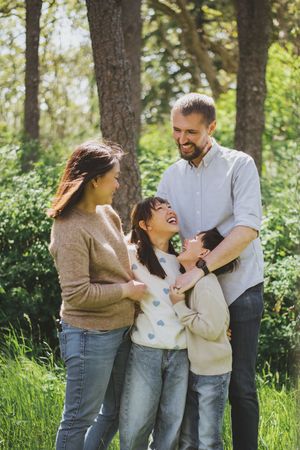 A family shares joyful moments together while playing and laughing in a sunlit forest setting.
