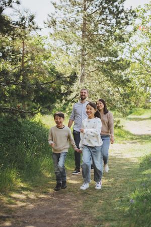A family walks together on a winding dirt path through green grass and trees on a sunny day.