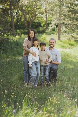 Family sitting together on grassy meadow with wildflowers on sunny spring day.