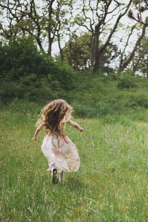 A child in a white dress twirls and dances through a sunny wildflower meadow on a summer afternoon.
