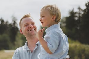 A parent and child share a joyful moment together outdoors on a sunny day with trees in the background.