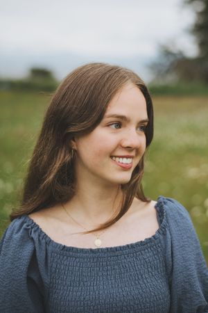 A person wearing a dark blue smocked top smiles while posing in a grassy outdoor field.