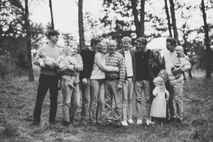 A vintage black and white photograph shows a group of people gathered outdoors with a bicycle in a wooded setting.