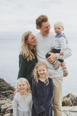 A family enjoys a playful moment together on a rocky beach shore with casual attire and natural lighting.