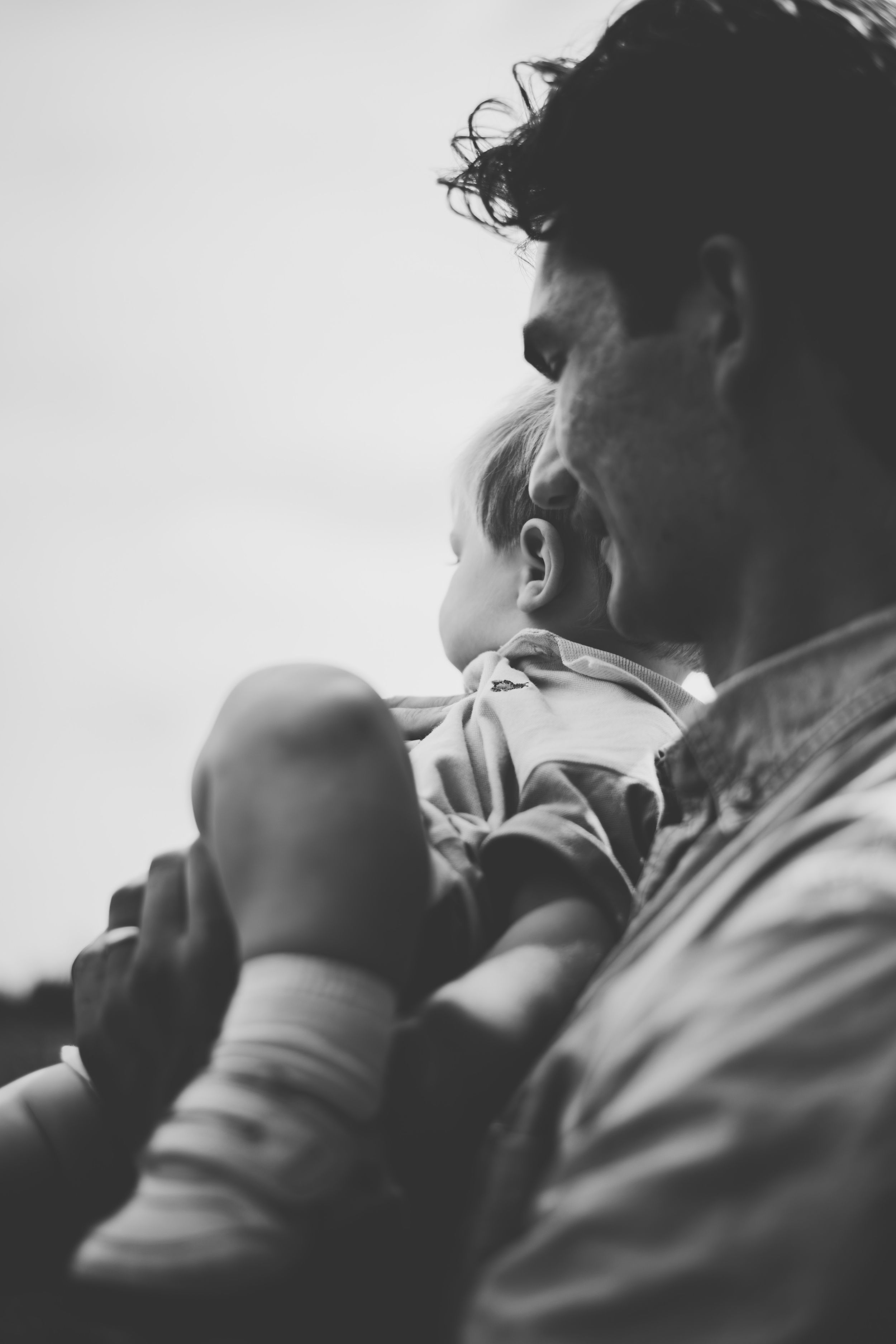 Black and white photo of a father tenderly holding his baby close, both gazing into the distance.