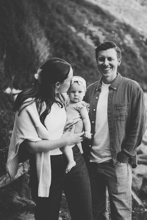 Black and white photo of a smiling family with mother kissing baby held by laughing father outdoors.