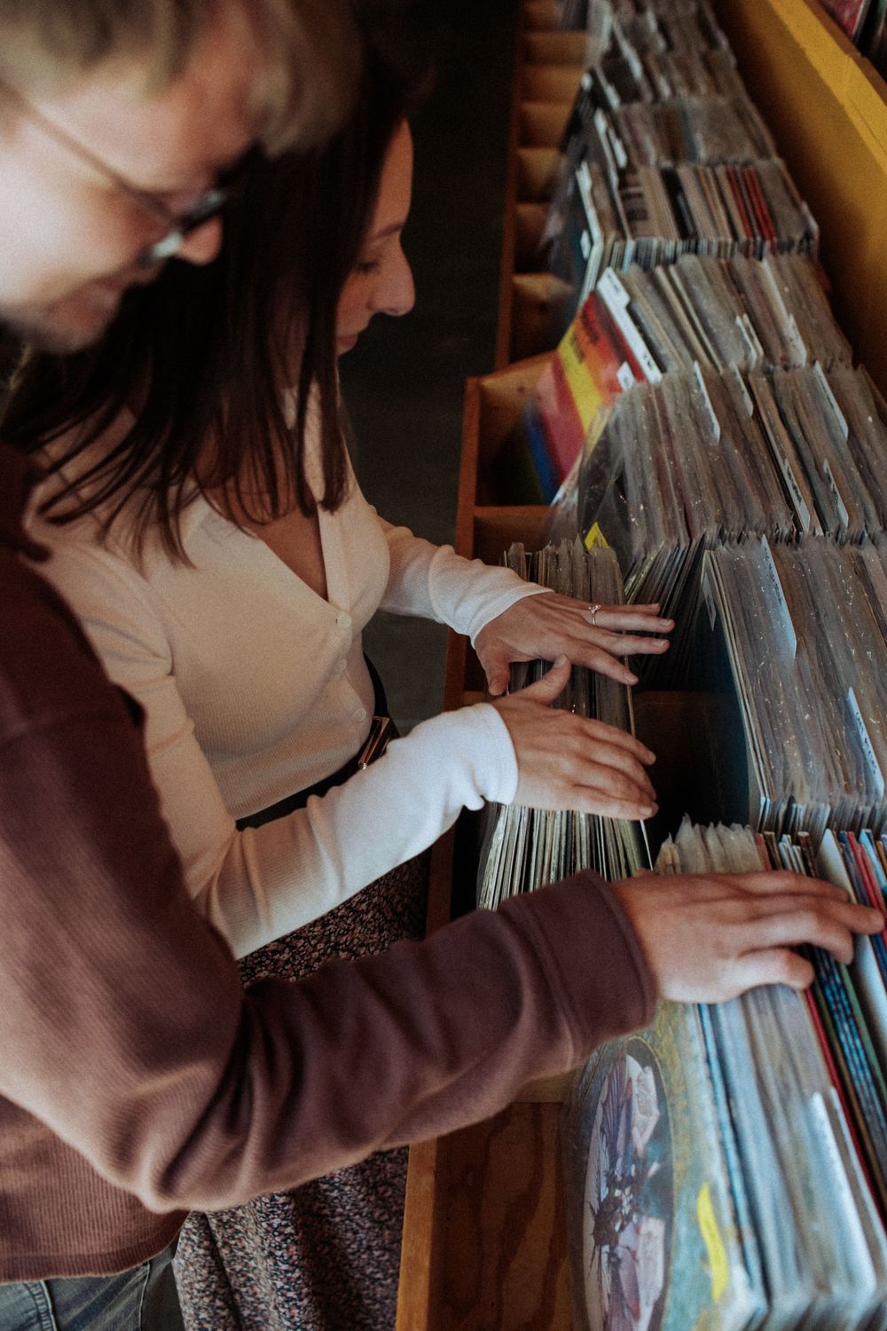 Someone flips through vinyl records in a record store while wearing a brown sweater and patterned skirt. Indianapolis, Indiana engagement se
