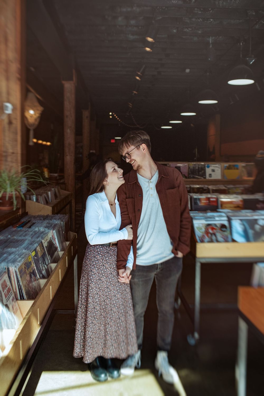 A couple shares a tender moment while browsing in a dimly lit record store.