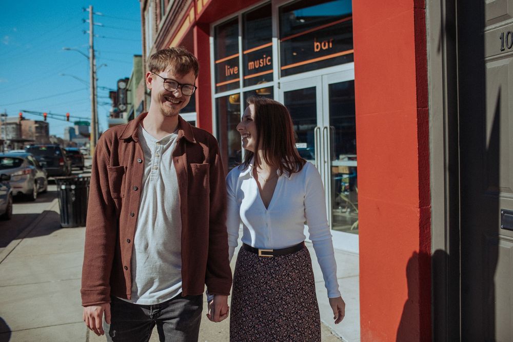 A couple stands together outside a building with bright red walls.