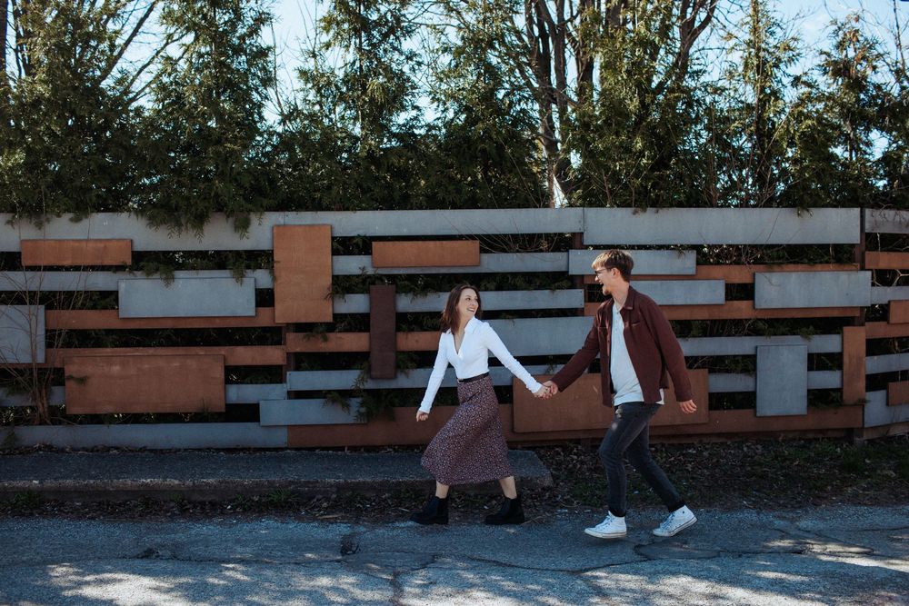 Two people walk together on a sunny day with trees in the background.
