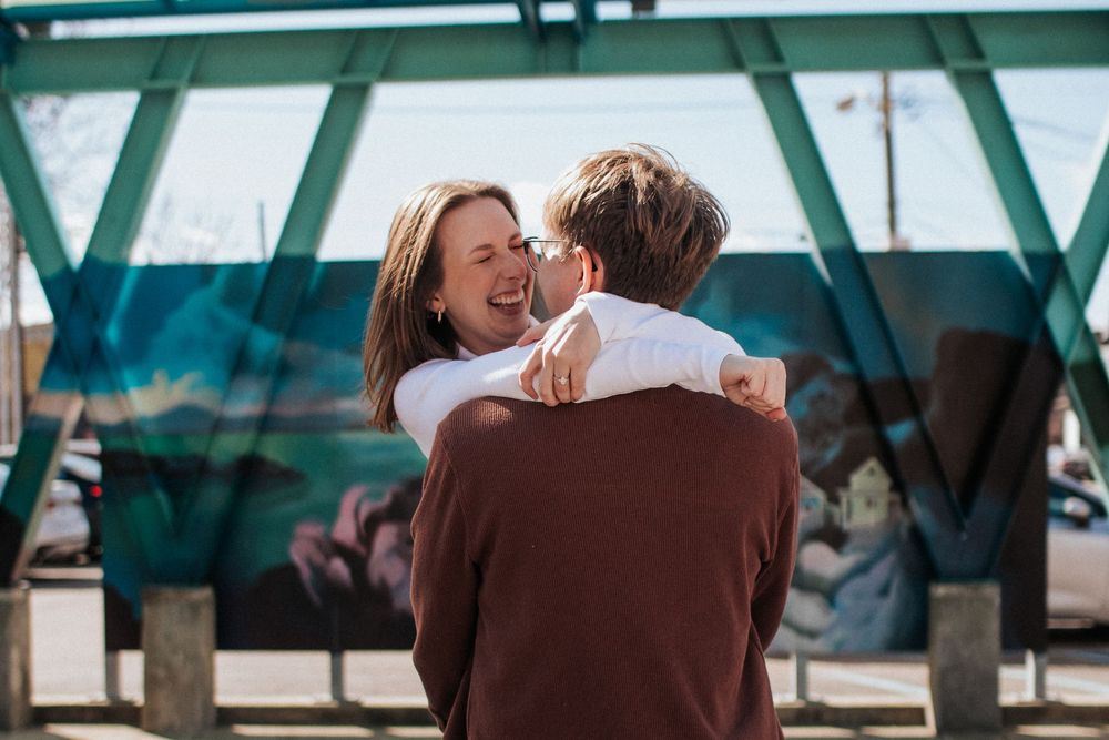 A romantic couple shares an intimate moment under a turquoise-tinted glass ceiling structure.