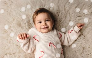 Baby girl wearing a candy cane sweater smiles as she lies on a warm white flokati, captured by Charlottesville maternity photographer.
