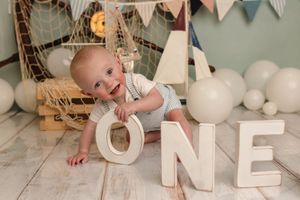 One year-old boy plays with the word "one" during his nautical-themed cake smash session with Charlottesville baby and newborn photographer.