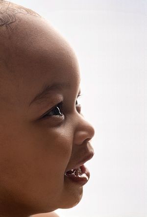 Backlit side profile detail shot of a laughing baby girl with dark eyes, captured by Charlottesville family and maternity photographer.