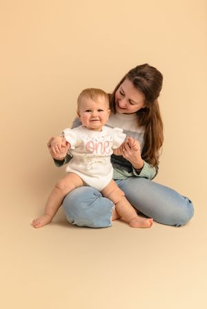 Baby girl in a white sweater sits on her mom during her first birthday cake smash session at Charlottesville newborn photography studio.