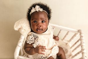 Three month-old baby girl wearing a cream boho romper sits in a white spindle cradle, smiling softly,  by Charlottesville photographer.