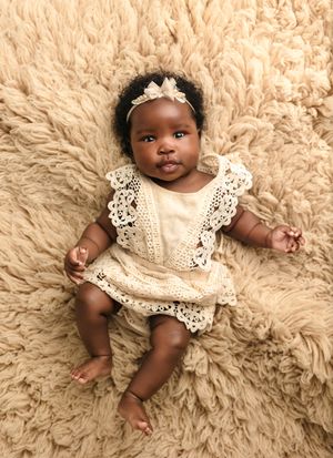 Bright-eyed baby wearing a lacy boho romper lies against a beige wool rug, captured by Charlottesville maternity photographer.