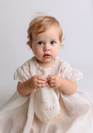 Baby girl in an antique white dress holds a vintage handkerchief for her one-year milestone session by Charlottesville family photographer.