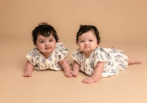 Twin six month-old sisters smile at the camera, dressed in matching blue floral dresses, captured by Charlottesville baby photographer.