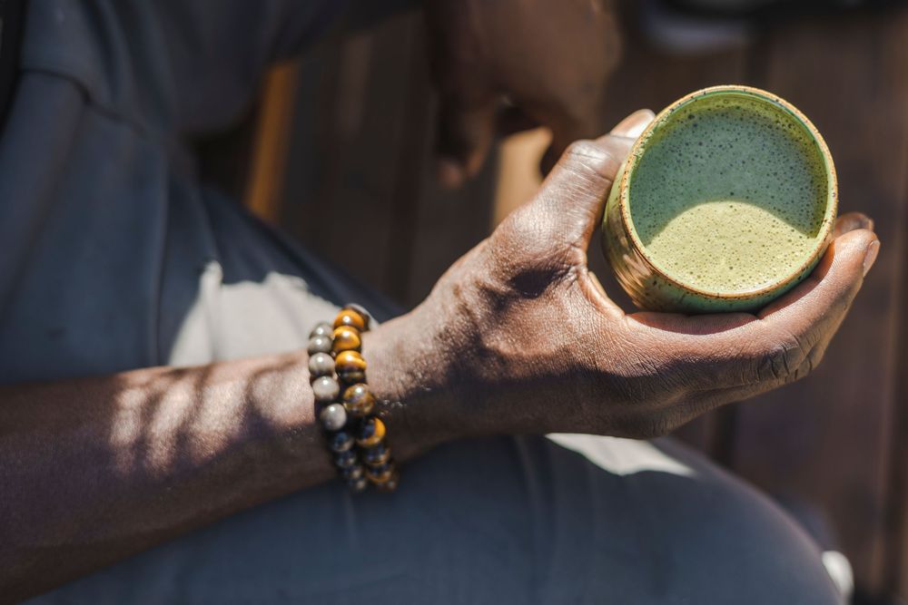 Hand holding a bowl of vibrant green matcha tea against a dark background with soft lighting.