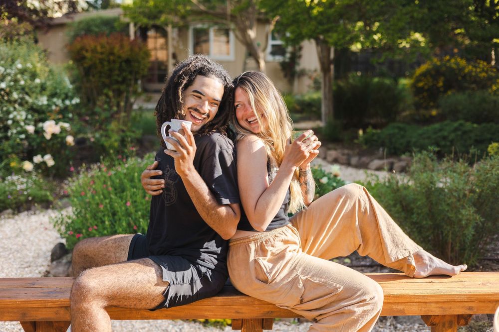 A couple shares a romantic moment together while sitting on a wooden bench in a lush garden setting.