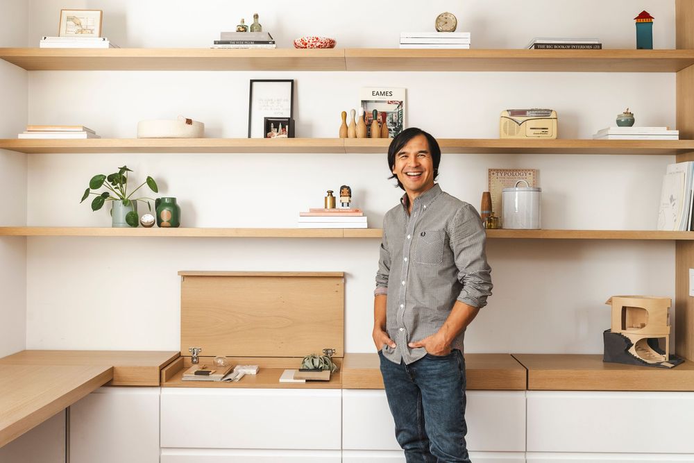 Modern home office with minimalist wooden floating shelves displaying decorative items and plants against white walls.
