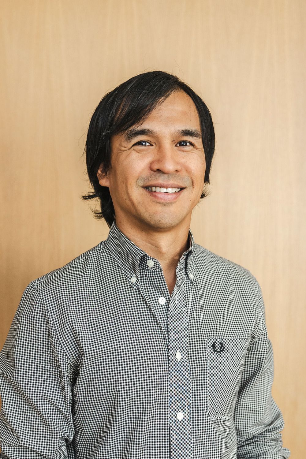 A person wearing a black and white gingham button-down shirt smiles warmly in a series of photos against a beige background.