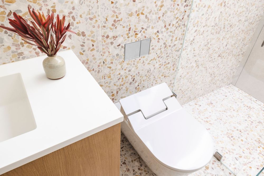 Modern bathroom with terrazzo wall tiles, white fixtures, and wooden vanity cabinet creates a sleek contemporary design.