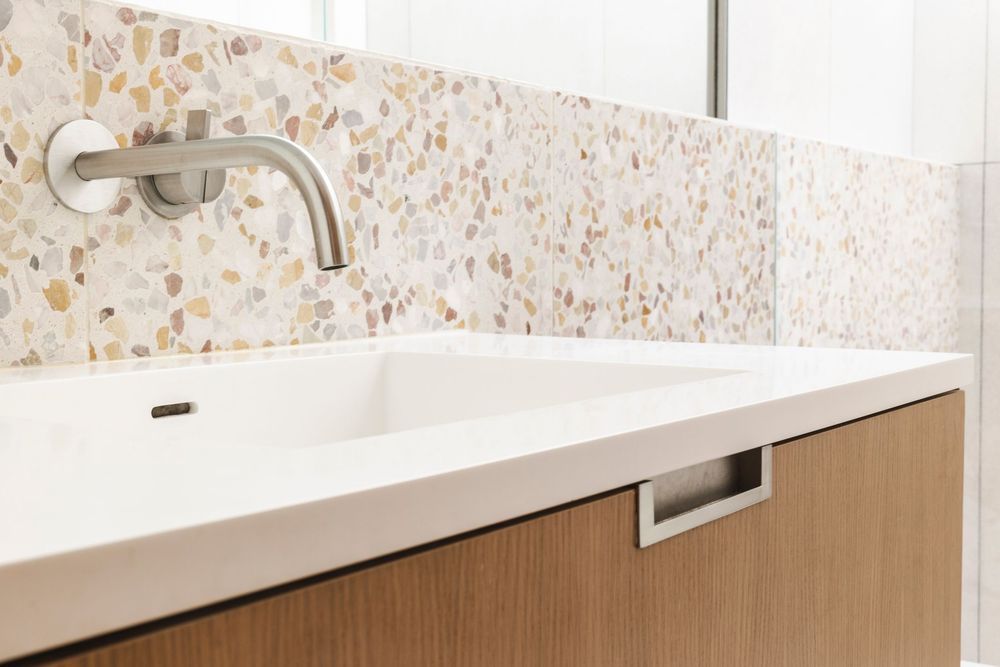 Modern bathroom interior with white terrazzo countertop, chrome faucet and speckled wall tiles in neutral tones.
