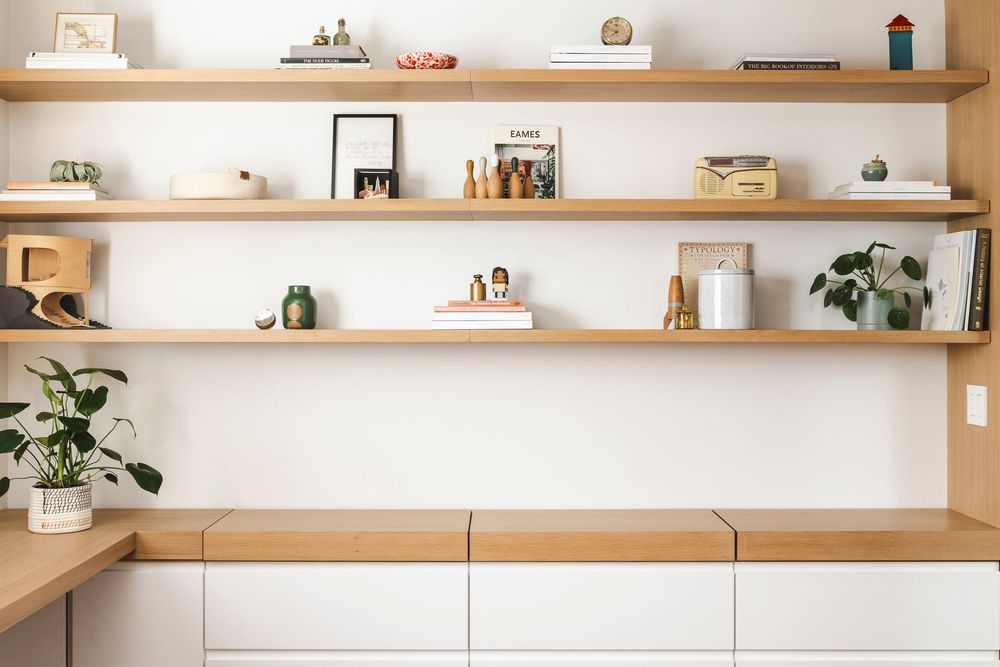 Minimalist white floating shelves display decorative items and plants against a white wall in a modern home interior.