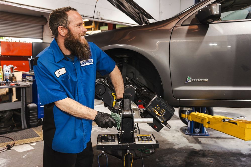 Automotive technician in blue uniform performs maintenance work on a vehicle in a professional service garage.