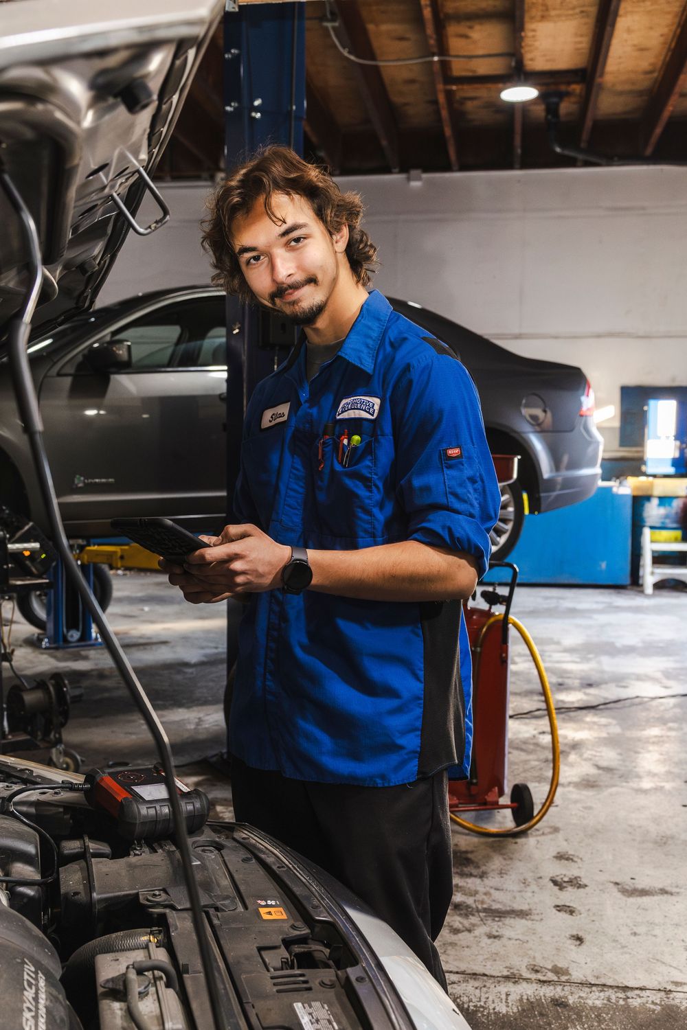 Auto mechanic in blue uniform performs maintenance work on a vehicle in a repair shop garage.