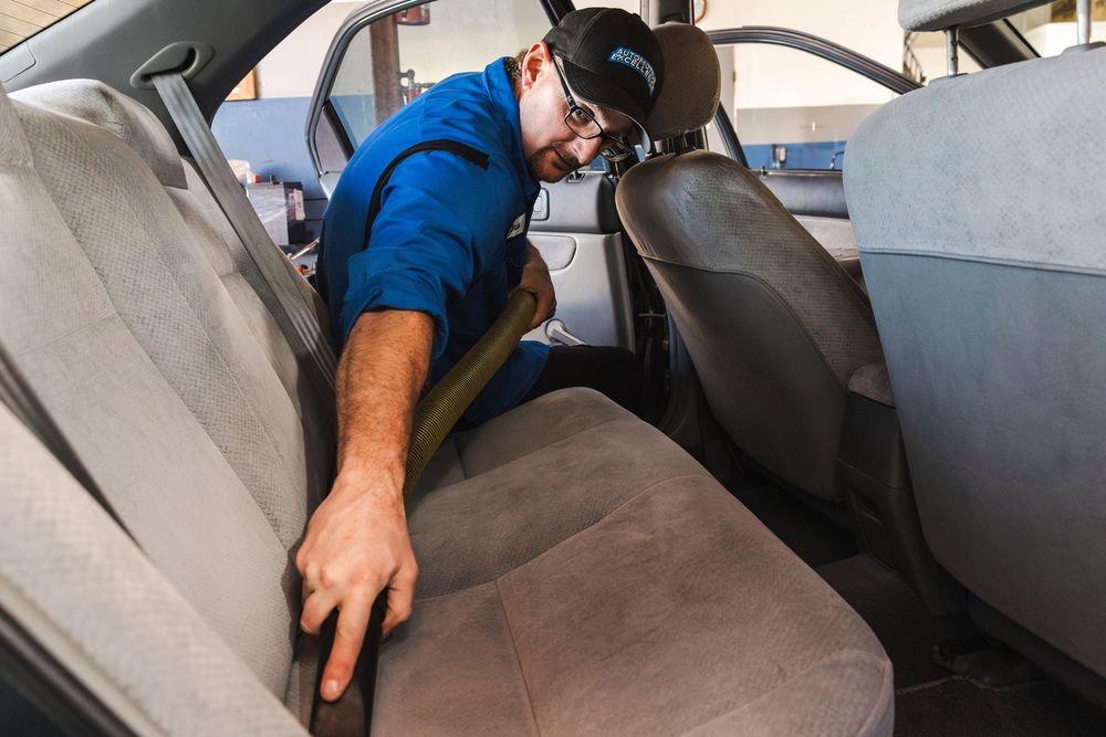 Professional auto detailer cleaning and vacuuming car interior seats and upholstery with specialized equipment.