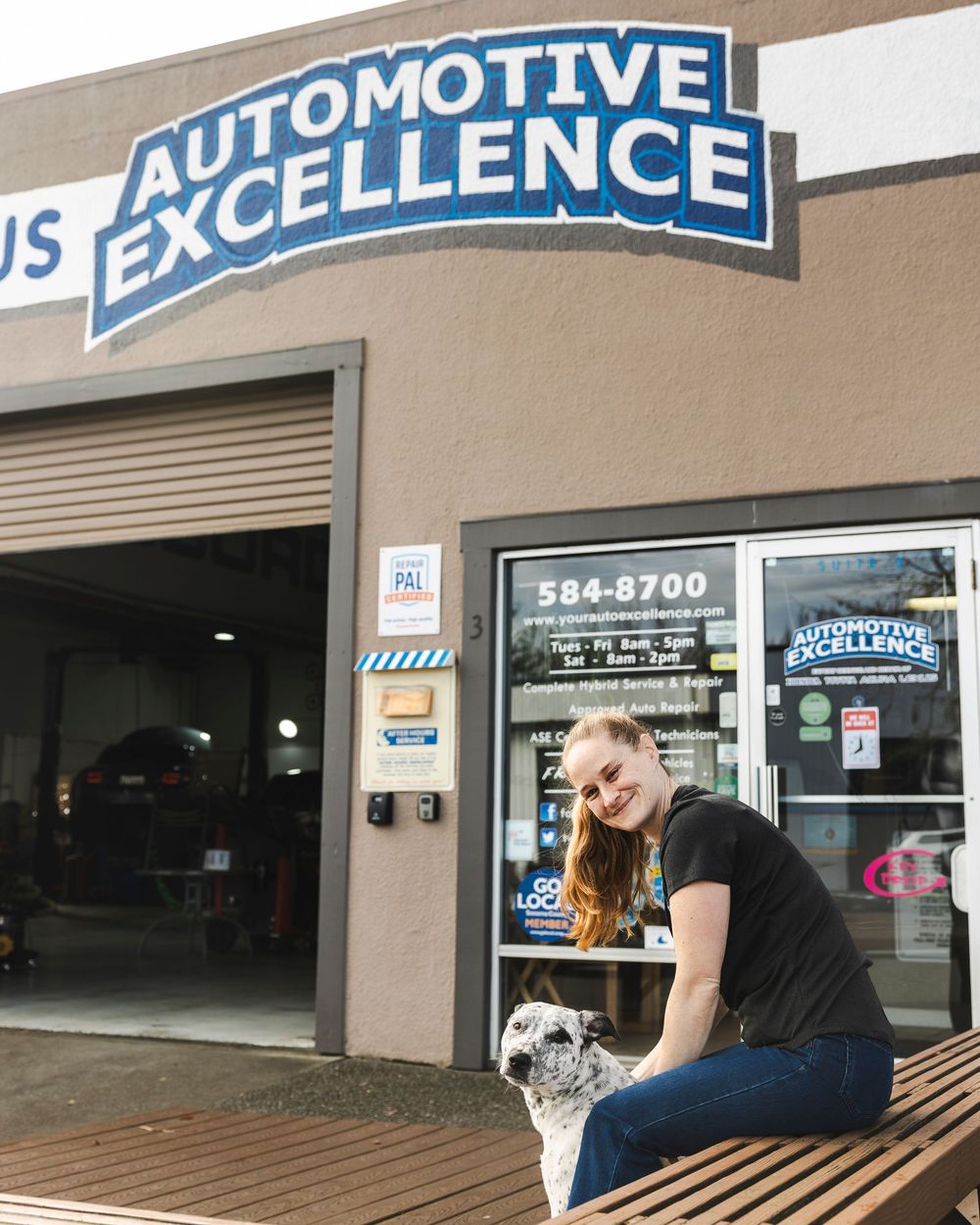 Automotive repair shop storefront with 'Excellence' signage and wooden bench seating outside.