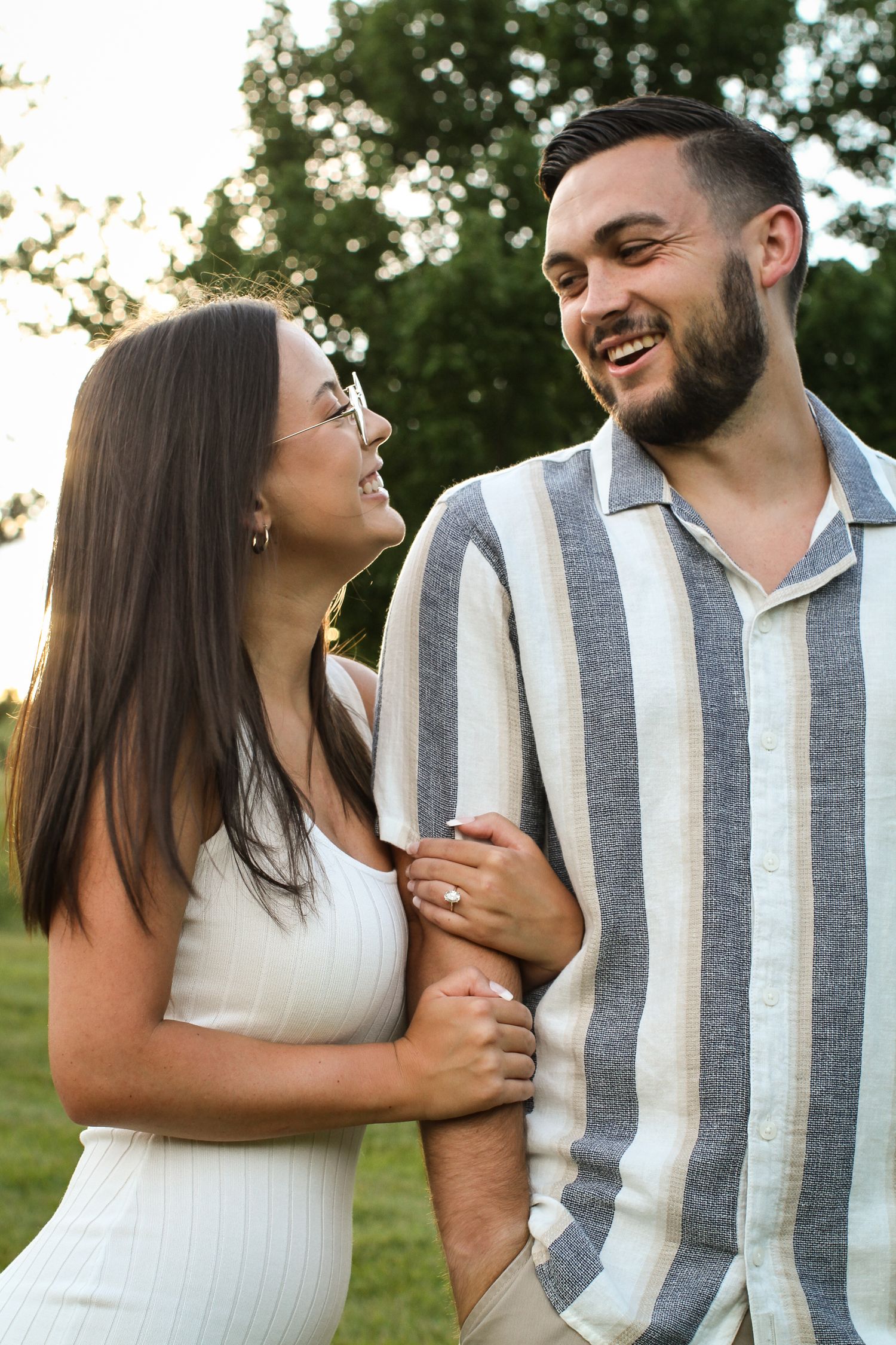 A woman beams at a man while holding his arm and showing off her diamond ring at a Kansas City engagement photo session.
