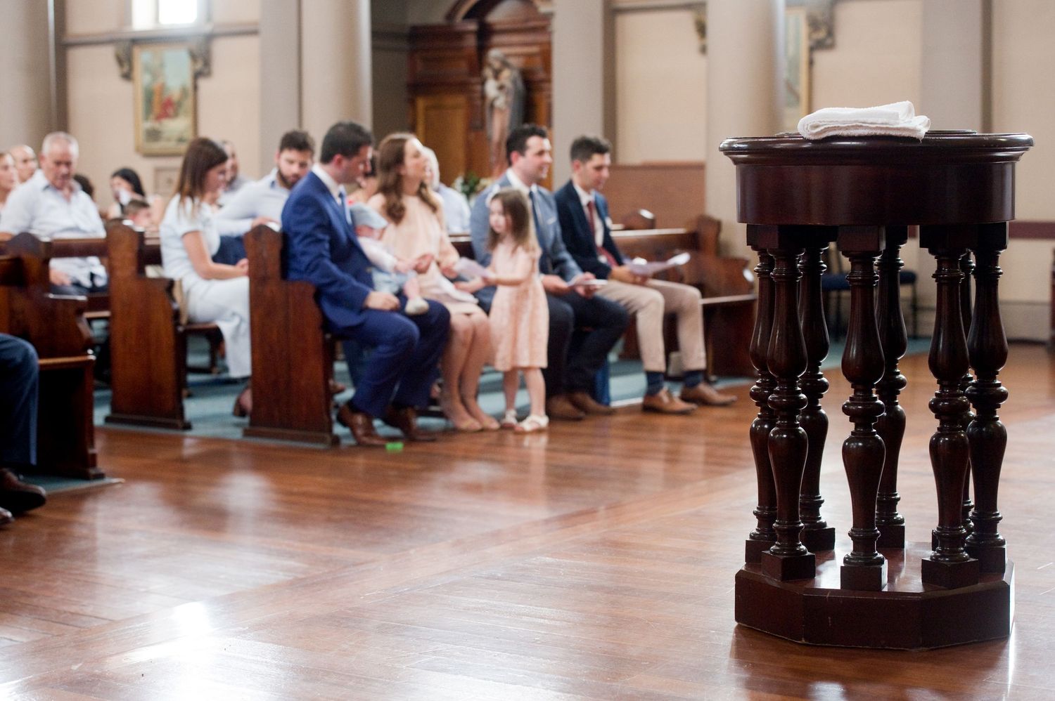 Wide view of church interior showing wooden pews and baptismal ceremony.