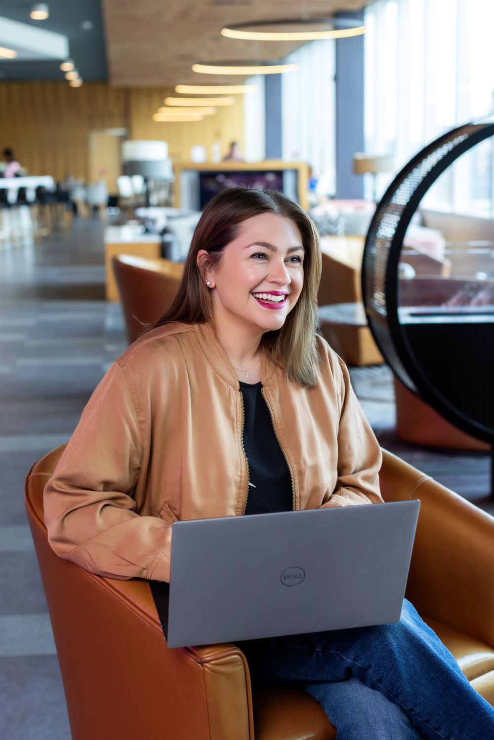 Professional working on Dell laptop in modern office space wearing tan blazer and black top.
