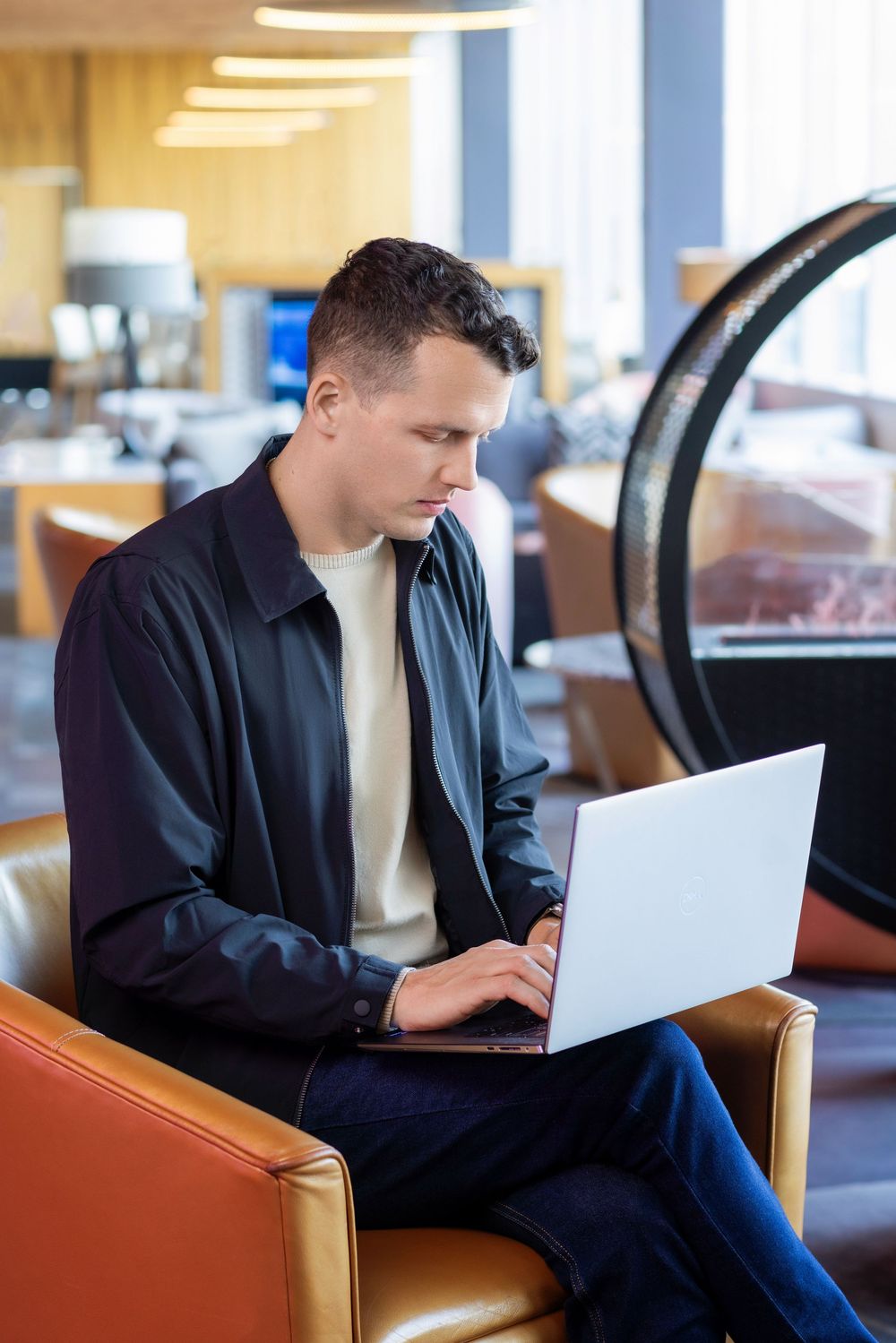 Person in dark clothing working on laptop computer in office setting with wooden furniture.