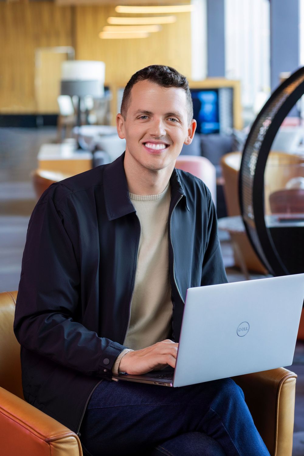 Professional working on Dell laptop in modern office setting with warm lighting and wooden furniture.