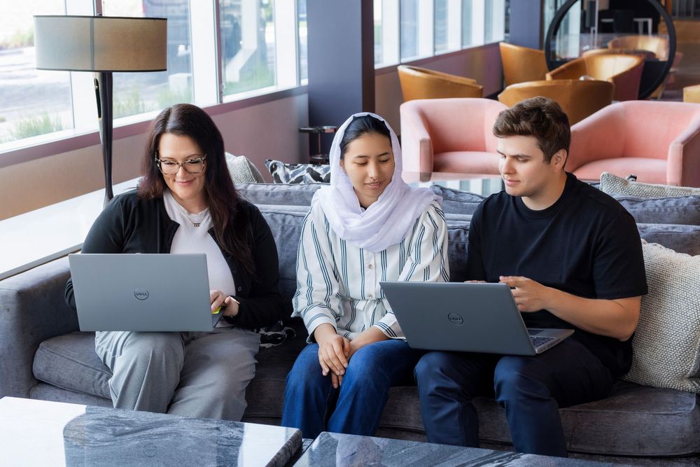 People working on laptops in a modern office space while sitting on comfortable couches and chairs.