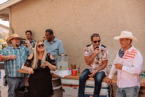 Group of guests mingling and socializing at an outdoor party with beige stucco walls in the background.
