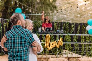 Couple hugging in garden setting decorated with teal balloons and festive string lights.