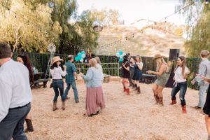 People dancing and mingling at an outdoor social gathering with string lights and desert landscape.
