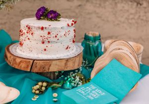 Multiple white frosted cakes displayed on wooden stands with turquoise table decor and floral arrangements.