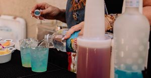 Colorful drinks being poured and served in glasses at an outdoor event.