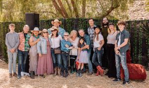 Large group photo of family members wearing coordinated casual outfits in pink, blue and denim against outdoor backdrop.